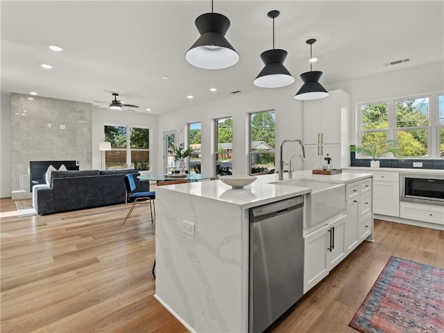 kitchen featuring a large fireplace, white cabinets, light wood-style floors, dishwasher, and an island with sink