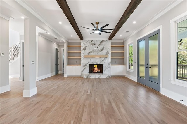 unfurnished living room featuring a high end fireplace, built in shelves, ornamental molding, beamed ceiling, and light hardwood / wood-style floors