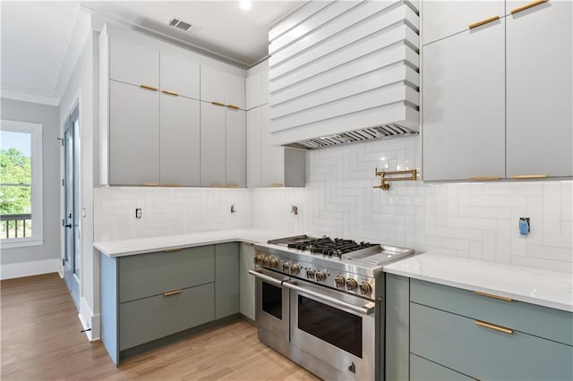 kitchen featuring light stone counters, light hardwood / wood-style flooring, backsplash, premium range hood, and range with two ovens