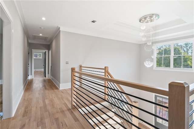 corridor with ornamental molding, light hardwood / wood-style floors, a tray ceiling, and a notable chandelier