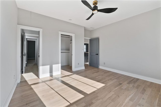 unfurnished bedroom with a closet, a walk in closet, light hardwood / wood-style floors, and ceiling fan