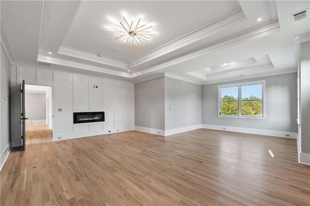 unfurnished living room featuring a tray ceiling, crown molding, and light hardwood / wood-style floors