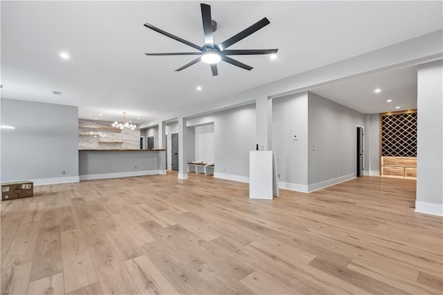 unfurnished living room featuring ceiling fan with notable chandelier and light hardwood / wood-style flooring