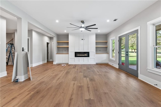 unfurnished living room with french doors, light hardwood / wood-style floors, ceiling fan, and built in shelves