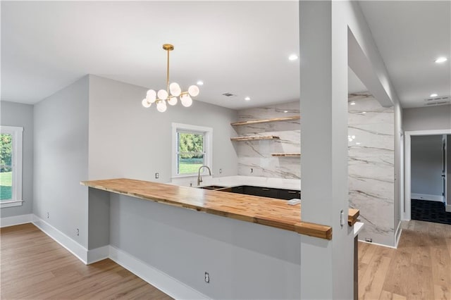 kitchen featuring sink, hanging light fixtures, light hardwood / wood-style flooring, kitchen peninsula, and a chandelier