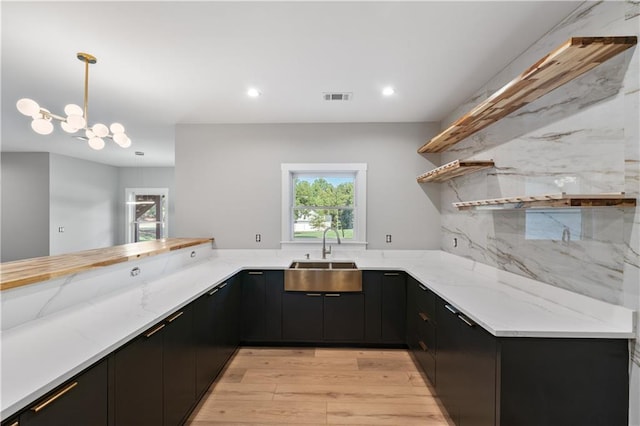 kitchen featuring pendant lighting, sink, decorative backsplash, light stone countertops, and kitchen peninsula