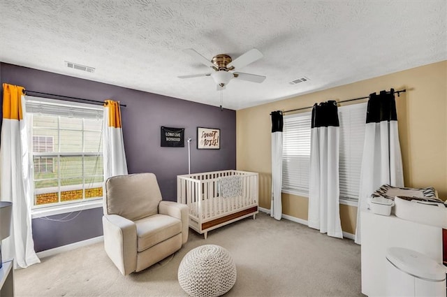 carpeted bedroom featuring ceiling fan, a crib, multiple windows, and a textured ceiling