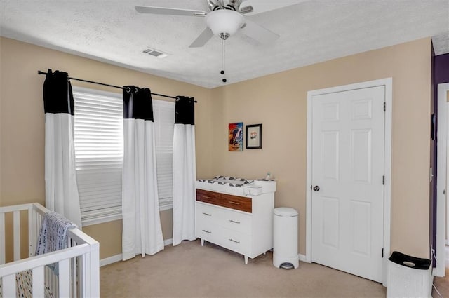 bedroom featuring light carpet, ceiling fan, a textured ceiling, and a crib