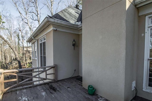 view of side of property featuring a shingled roof, a wooden deck, and stucco siding