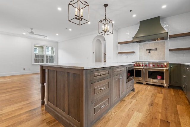 kitchen with light countertops, double oven range, wall chimney range hood, and open shelves