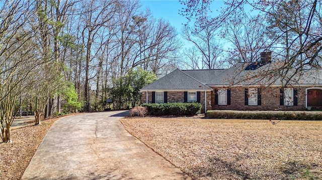 ranch-style house featuring concrete driveway, brick siding, and a chimney