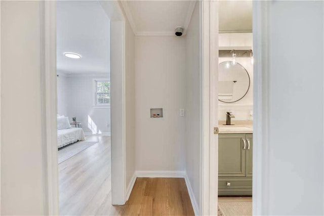 hall with a sink, baseboards, ornamental molding, and light wood-style flooring
