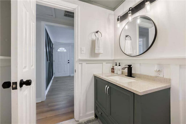 bathroom featuring vanity, visible vents, wood finished floors, a decorative wall, and a wainscoted wall