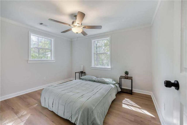 bedroom featuring a ceiling fan, baseboards, wood finished floors, visible vents, and ornamental molding