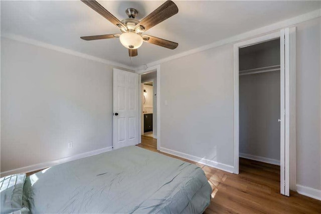 bedroom with a closet, ornamental molding, wood finished floors, baseboards, and ceiling fan