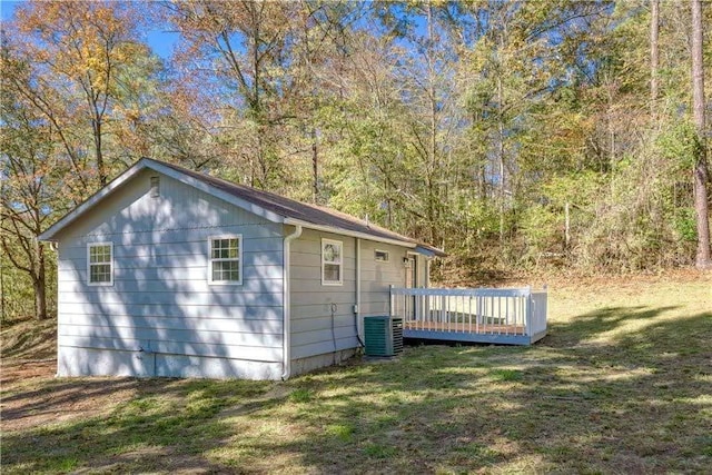 view of home's exterior featuring a lawn, a wooden deck, central air condition unit, and a wooded view