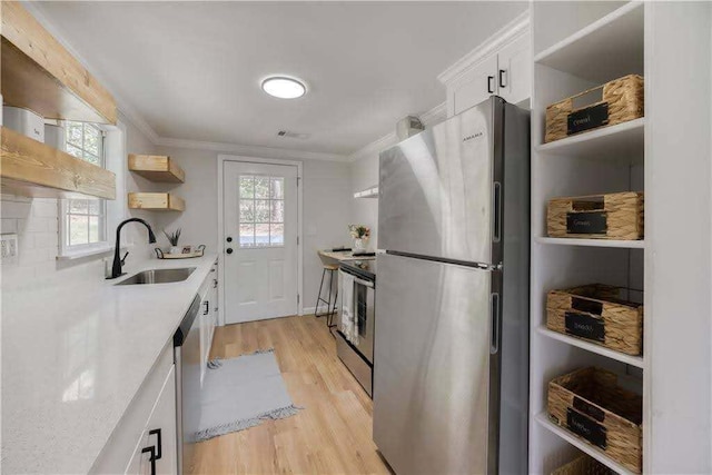 kitchen with open shelves, appliances with stainless steel finishes, a sink, light countertops, and light wood-style flooring