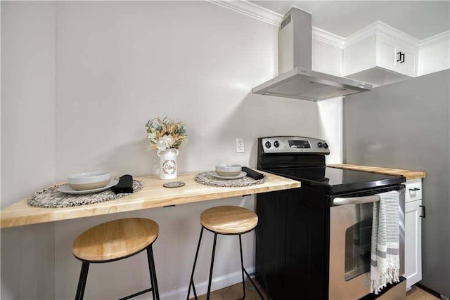 kitchen with wall chimney range hood, crown molding, a kitchen bar, and stainless steel range with electric stovetop