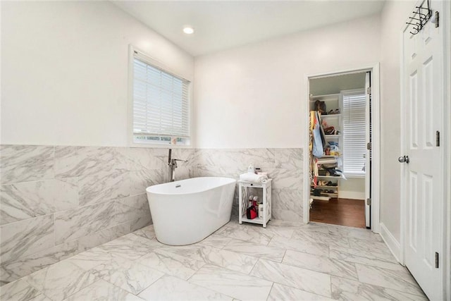 bathroom with a freestanding tub, tile walls, marble finish floor, and a wainscoted wall