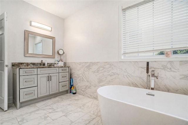 full bathroom featuring vanity, marble finish floor, wainscoting, tile walls, and a soaking tub