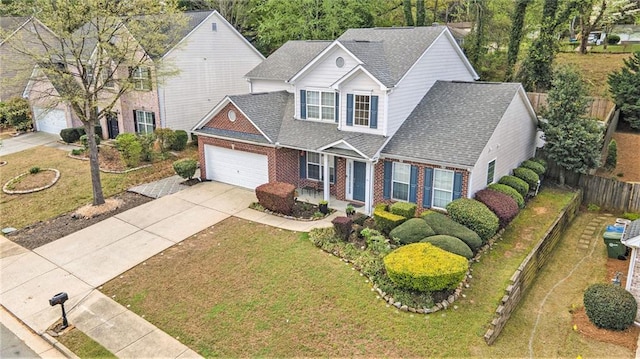 traditional-style house with a front yard, brick siding, fence, concrete driveway, and an attached garage