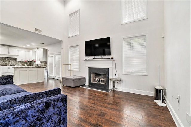 living area featuring visible vents, a fireplace with raised hearth, dark wood-type flooring, and a high ceiling