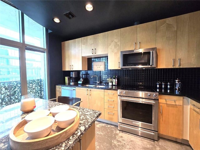 kitchen featuring light brown cabinets, sink, decorative backsplash, dark stone countertops, and appliances with stainless steel finishes