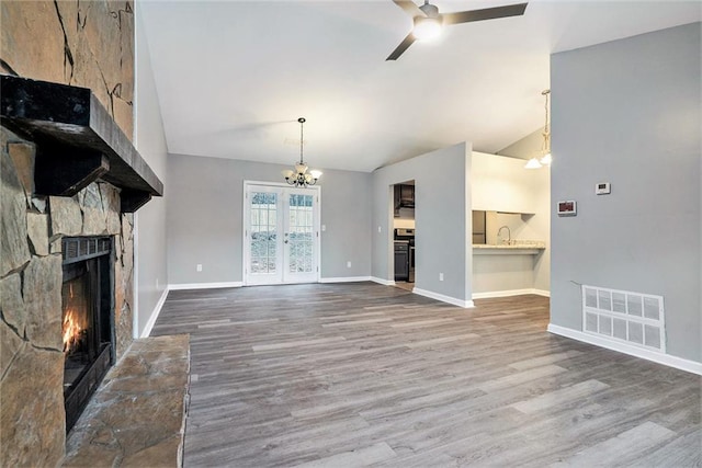 unfurnished living room featuring a fireplace, ceiling fan with notable chandelier, vaulted ceiling, and hardwood / wood-style flooring