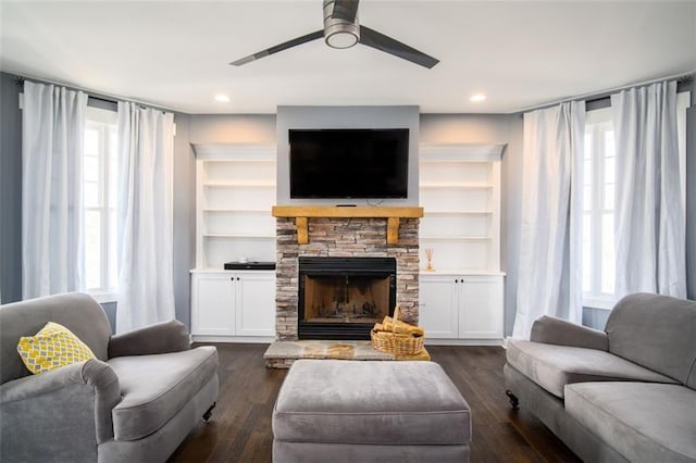 living area featuring a stone fireplace, dark wood-style floors, a healthy amount of sunlight, and a ceiling fan