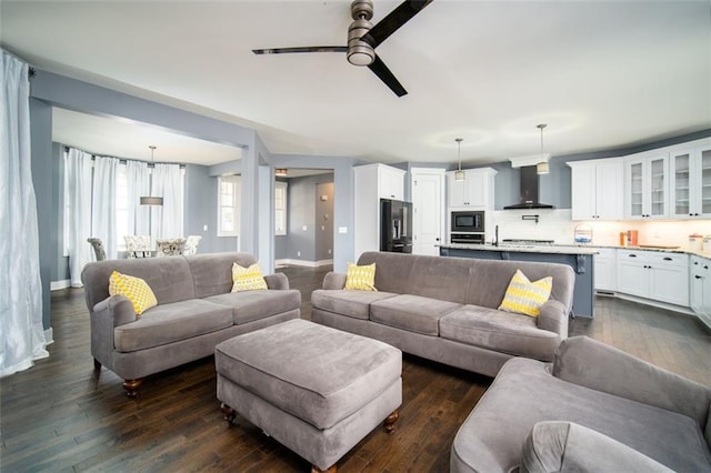 living area with dark wood-type flooring, baseboards, and ceiling fan