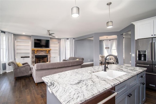 kitchen with a sink, light stone counters, appliances with stainless steel finishes, a ceiling fan, and dark wood-style flooring