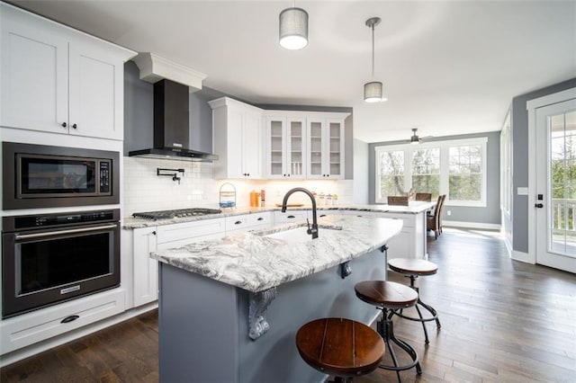 kitchen with a sink, backsplash, appliances with stainless steel finishes, and wall chimney range hood