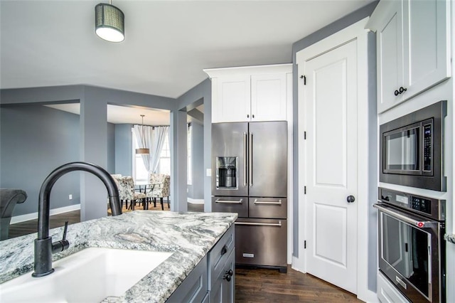 kitchen with light stone counters, dark wood-style floors, white cabinets, stainless steel appliances, and a sink