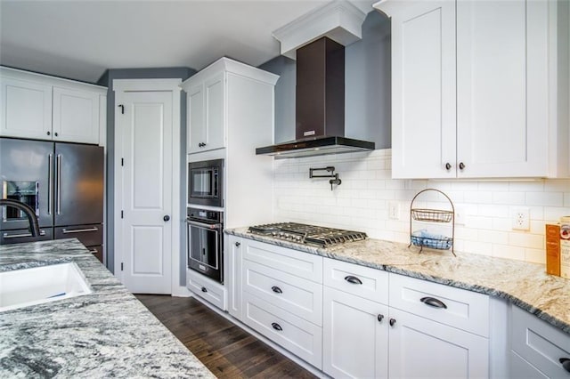 kitchen featuring light stone countertops, appliances with stainless steel finishes, white cabinetry, wall chimney exhaust hood, and a sink