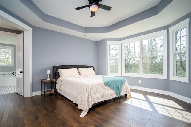 bedroom featuring dark wood-style floors, multiple windows, a raised ceiling, and baseboards