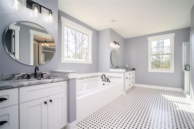 full bath featuring two vanities, a sink, a bath, baseboards, and a chandelier