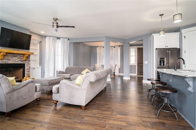 living area featuring plenty of natural light, a stone fireplace, ceiling fan, and dark wood-style flooring