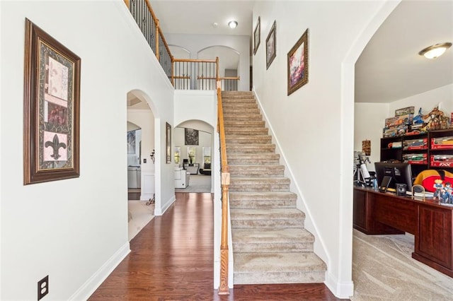 stairs with hardwood / wood-style floors and a high ceiling