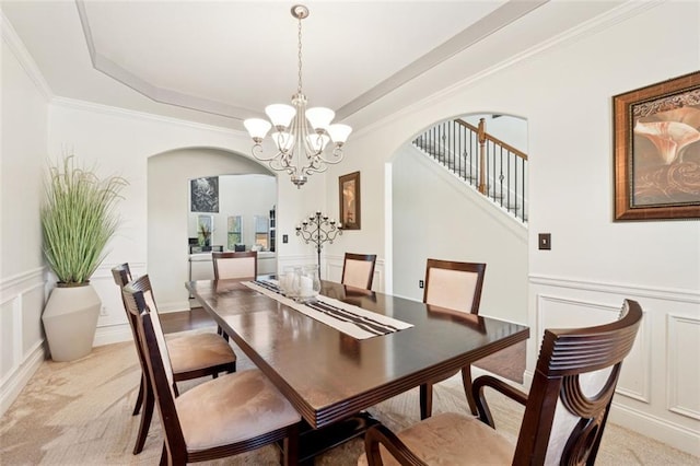 carpeted dining room with an inviting chandelier, ornamental molding, and a raised ceiling