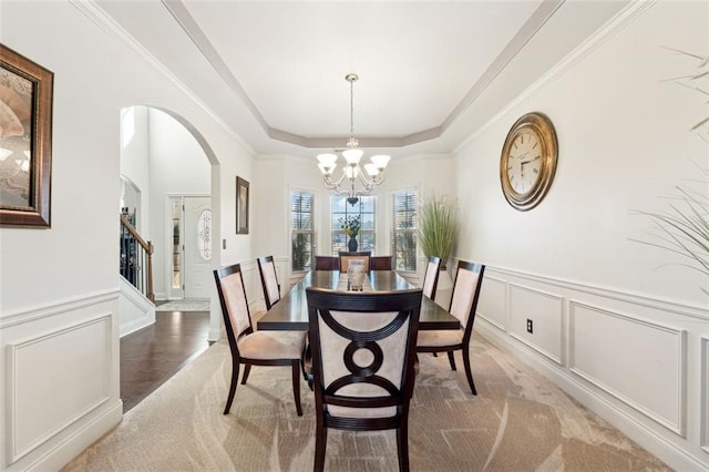 carpeted dining room featuring an inviting chandelier, ornamental molding, and a raised ceiling