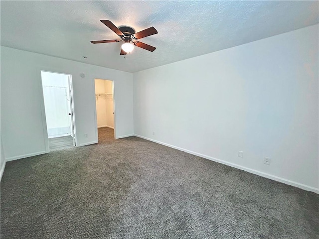 unfurnished bedroom with dark colored carpet, a spacious closet, a textured ceiling, a closet, and ceiling fan