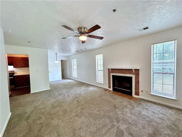 unfurnished living room featuring ceiling fan, a tile fireplace, a textured ceiling, and carpet flooring