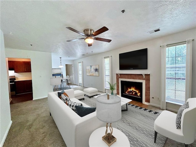 living room featuring a tiled fireplace, ceiling fan, a textured ceiling, and carpet