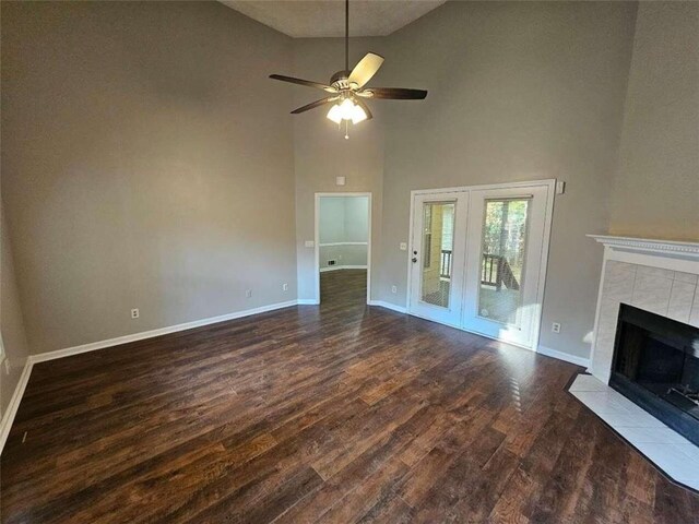 unfurnished living room featuring a tiled fireplace, high vaulted ceiling, dark wood-type flooring, and ceiling fan