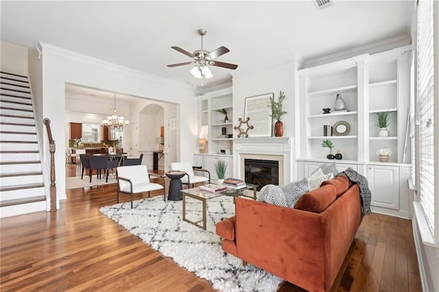 living room with crown molding, ceiling fan with notable chandelier, built in features, and light hardwood / wood-style flooring