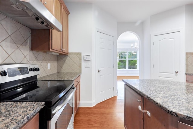 3690 Dalwood Dr, Suwanee, GA 30024 - kitchen featuring stainless steel electric range, a notable chandelier, wall chimney range hood, decorative backsplash, and light hardwood / wood-style floors