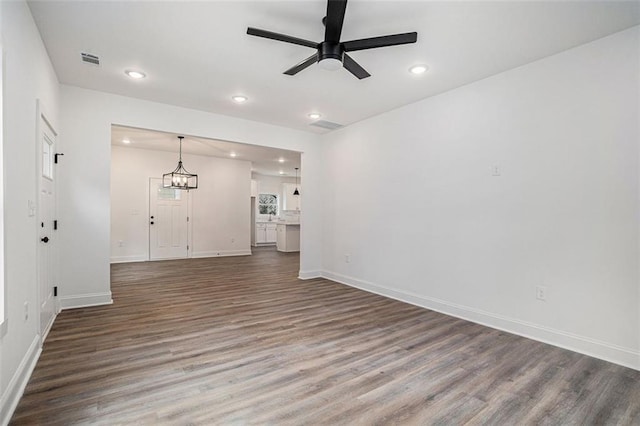 unfurnished living room with wood finished floors, visible vents, baseboards, and ceiling fan with notable chandelier