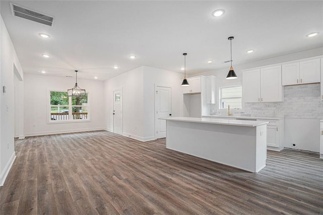 kitchen with white cabinets, dark wood-style flooring, a center island, and visible vents