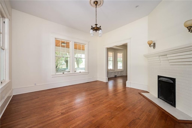 unfurnished living room with dark wood-type flooring, a fireplace, and a notable chandelier