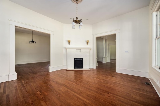 unfurnished living room featuring a notable chandelier, a fireplace, and dark hardwood / wood-style floors